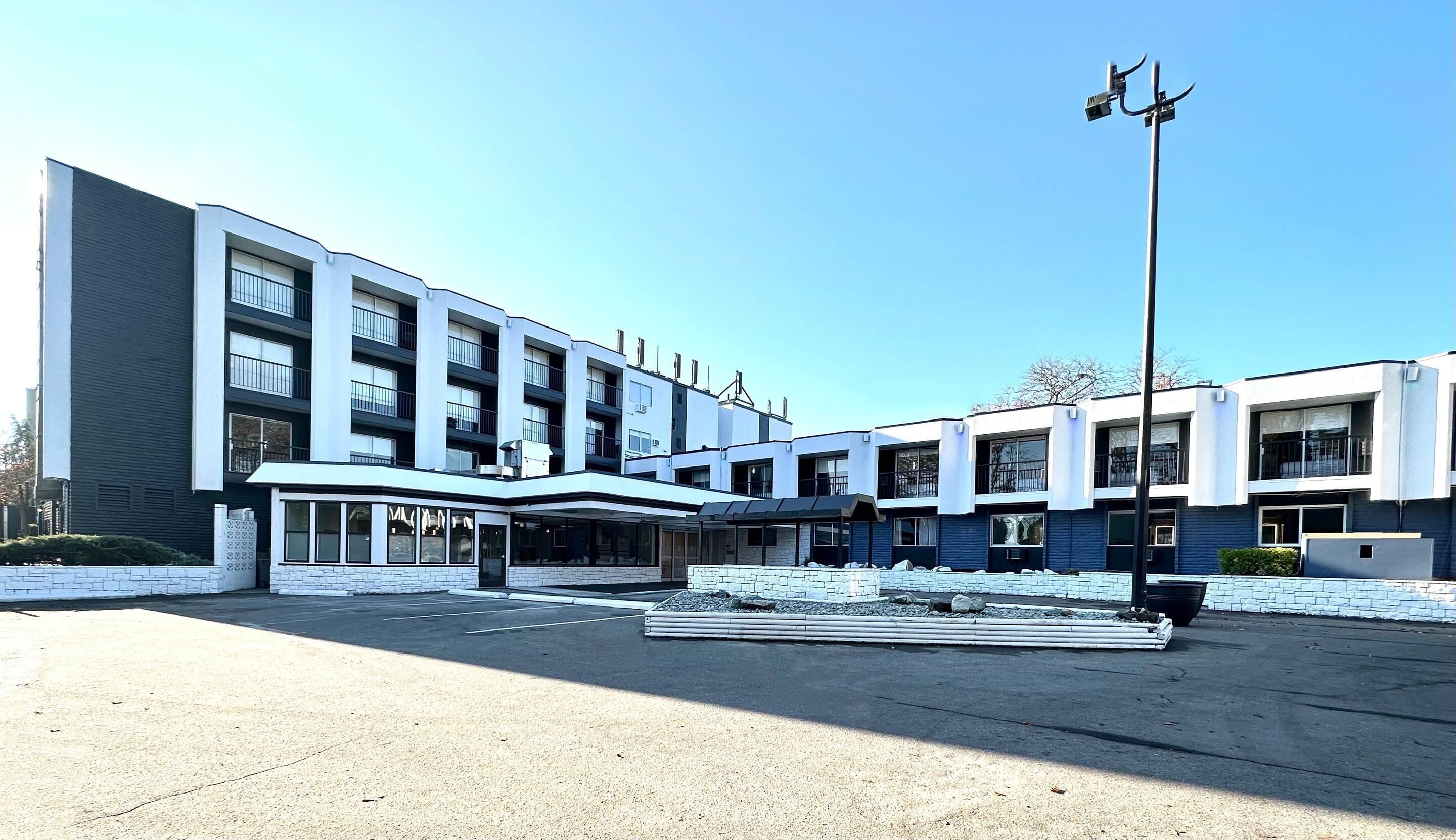 A modern multi-story building with a central entrance, large windows, and a parking area.
