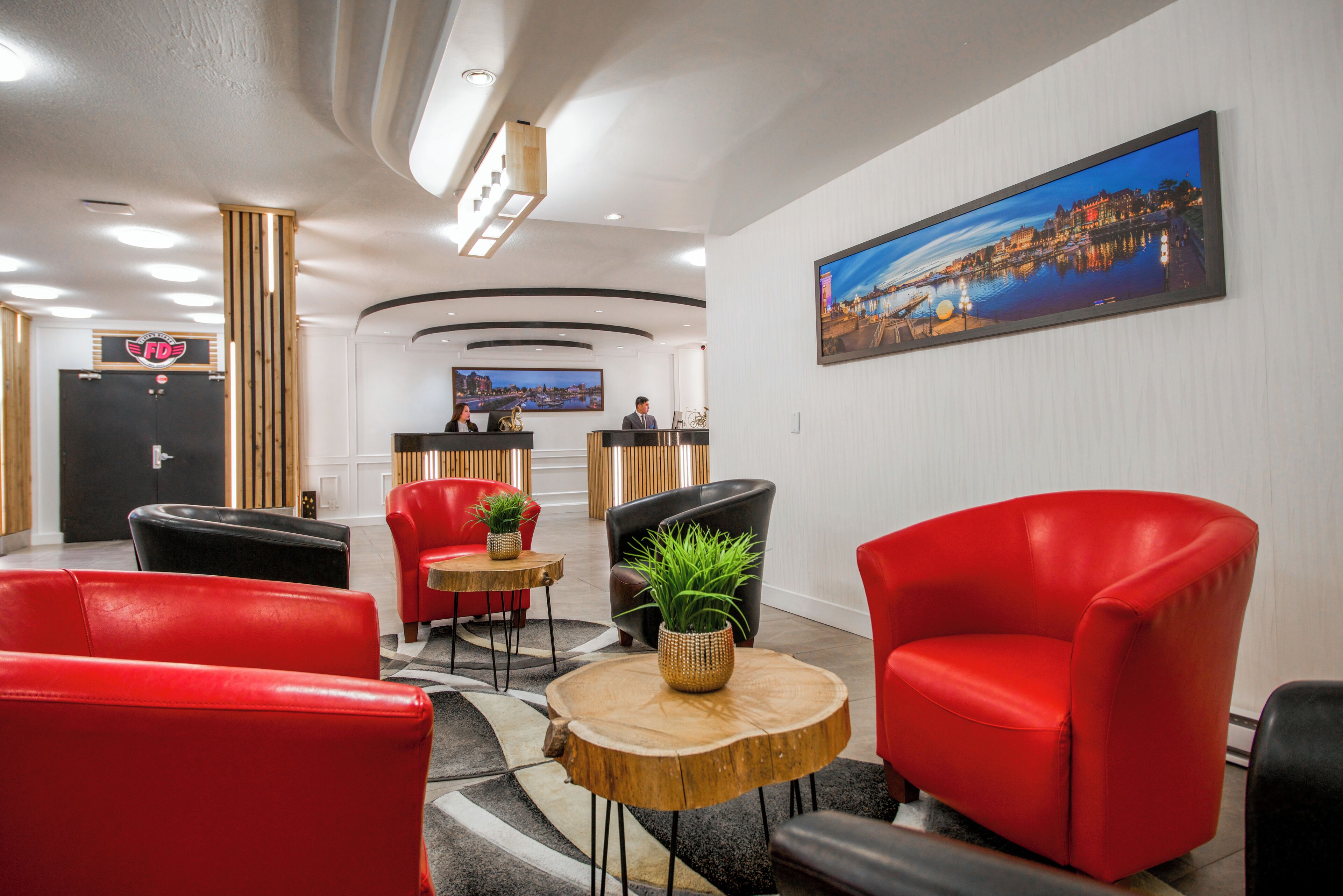 A hotel lobby with red leather chairs, a reception desk, a large cityscape painting, and a wooden coffee table with a plant.