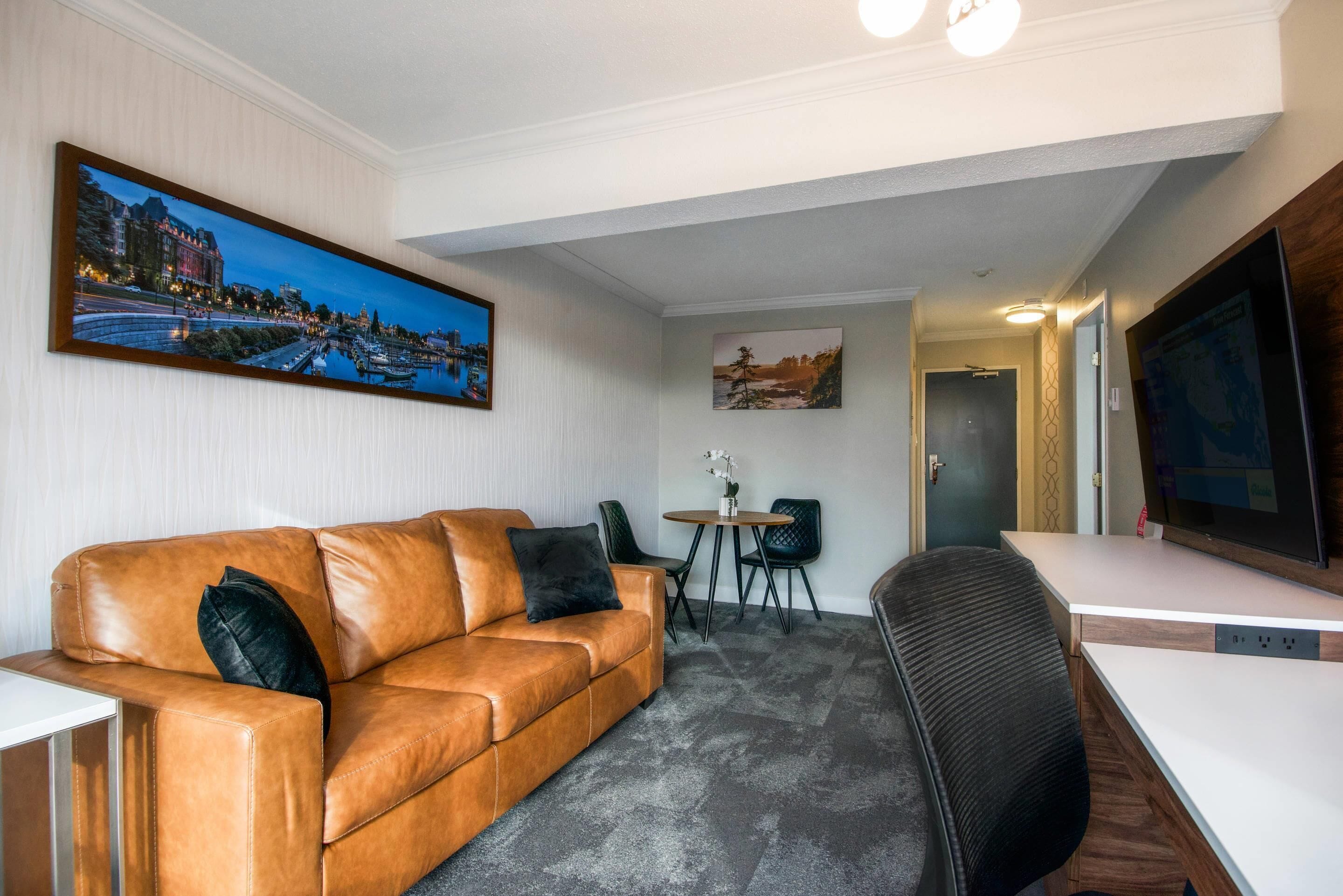 Une chambre moderne avec un canapé en cuir, une petite table avec des chaises, un bureau et un grand téléviseur à écran plat.