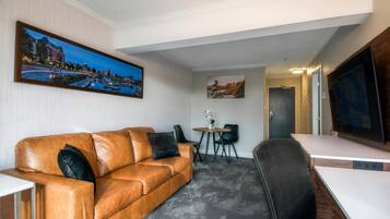 Une chambre moderne avec un canapé en cuir, une petite table avec des chaises, un bureau et un grand téléviseur à écran plat.