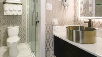 Une salle de bain comprenant des toilettes, un espace de douche vitré, un lavabo avec un receveur métallique et un porte-serviettes avec des serviettes pliées.