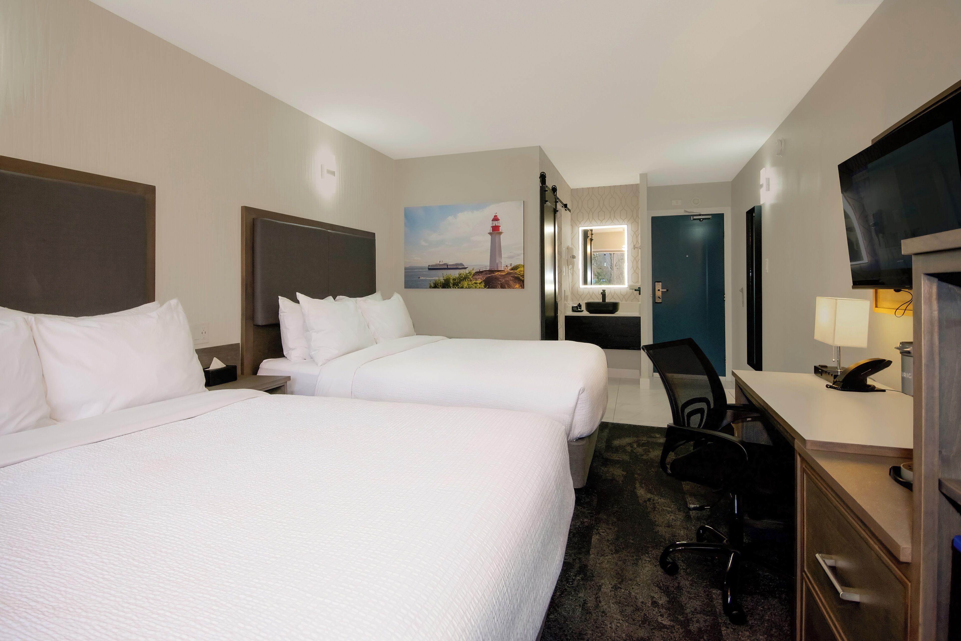 Habitación de hotel con dos camas, un escritorio, una silla, un televisor y un cuadro de un faro.