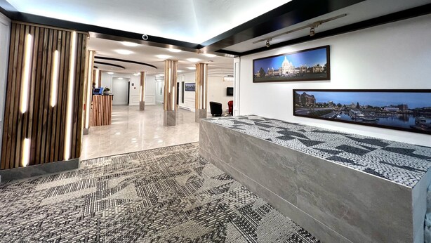 A modern hotel lobby with a reception desk, patterned carpet, and framed cityscape pictures on the wall. - The Vic, an Ascend Collection Hotel (Victoria)