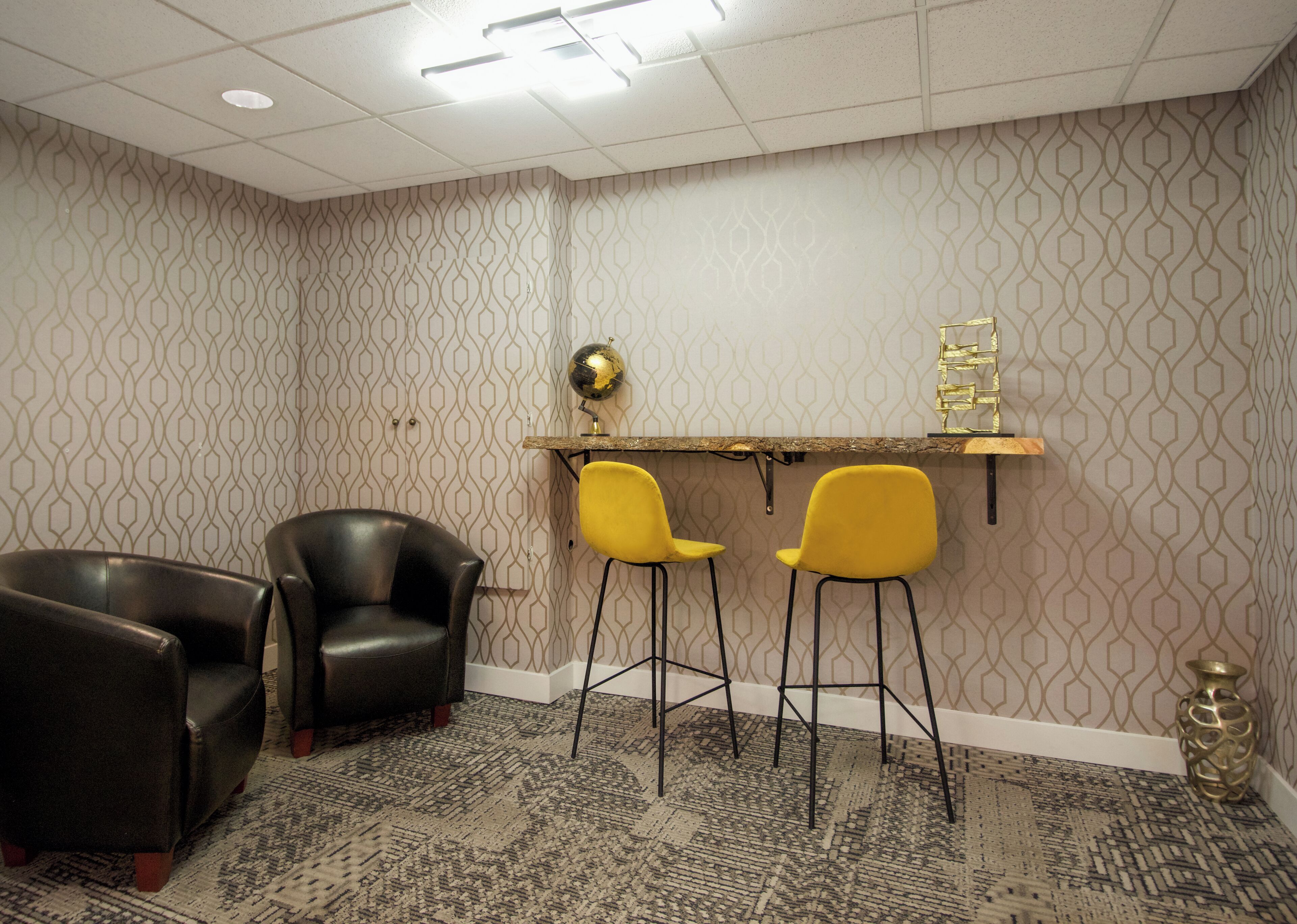 A room with patterned wallpaper, a globe on a shelf, two yellow chairs, and a black leather chair.
