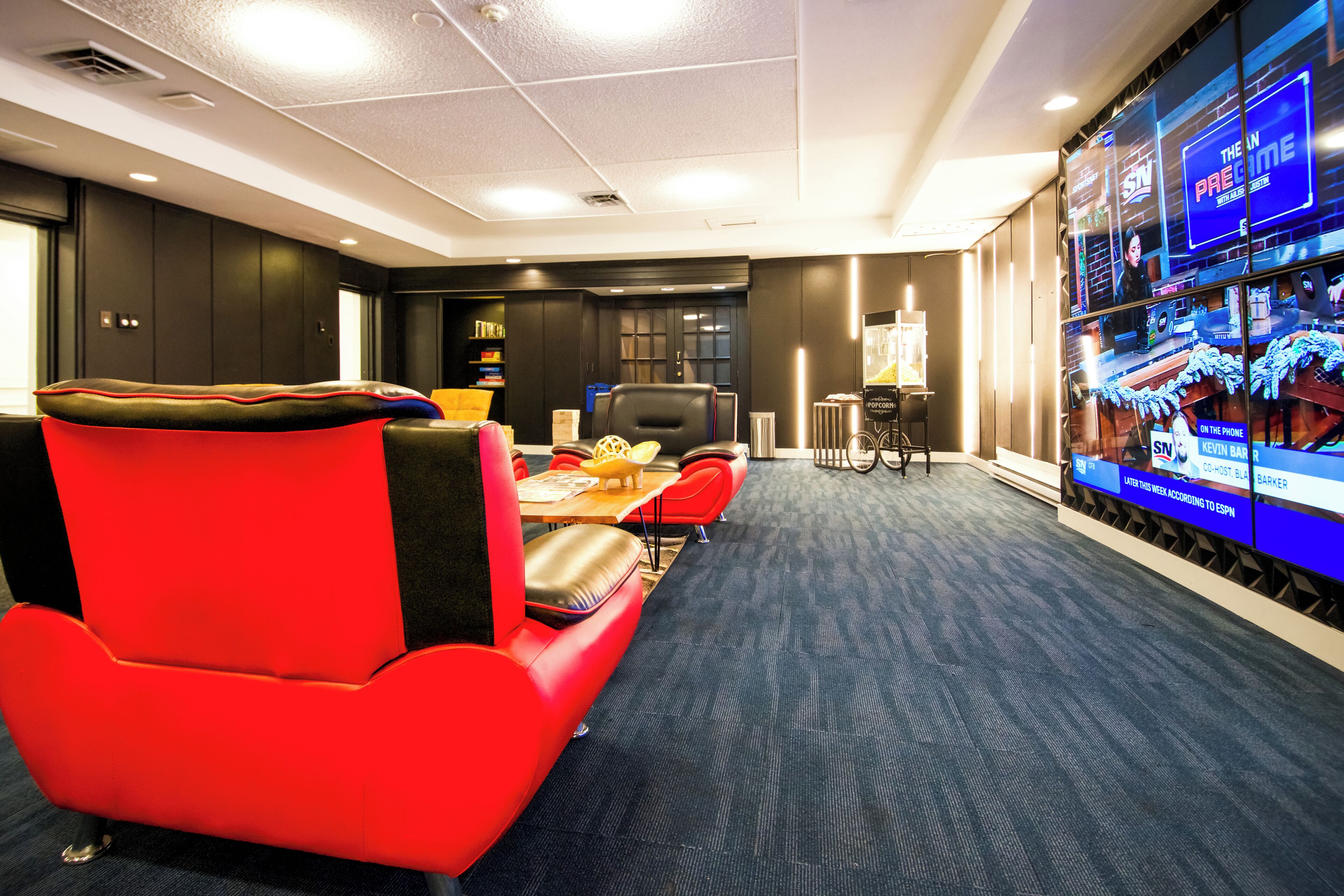 A conference room with a red chair, a table, and a TV screen displaying a sports channel.