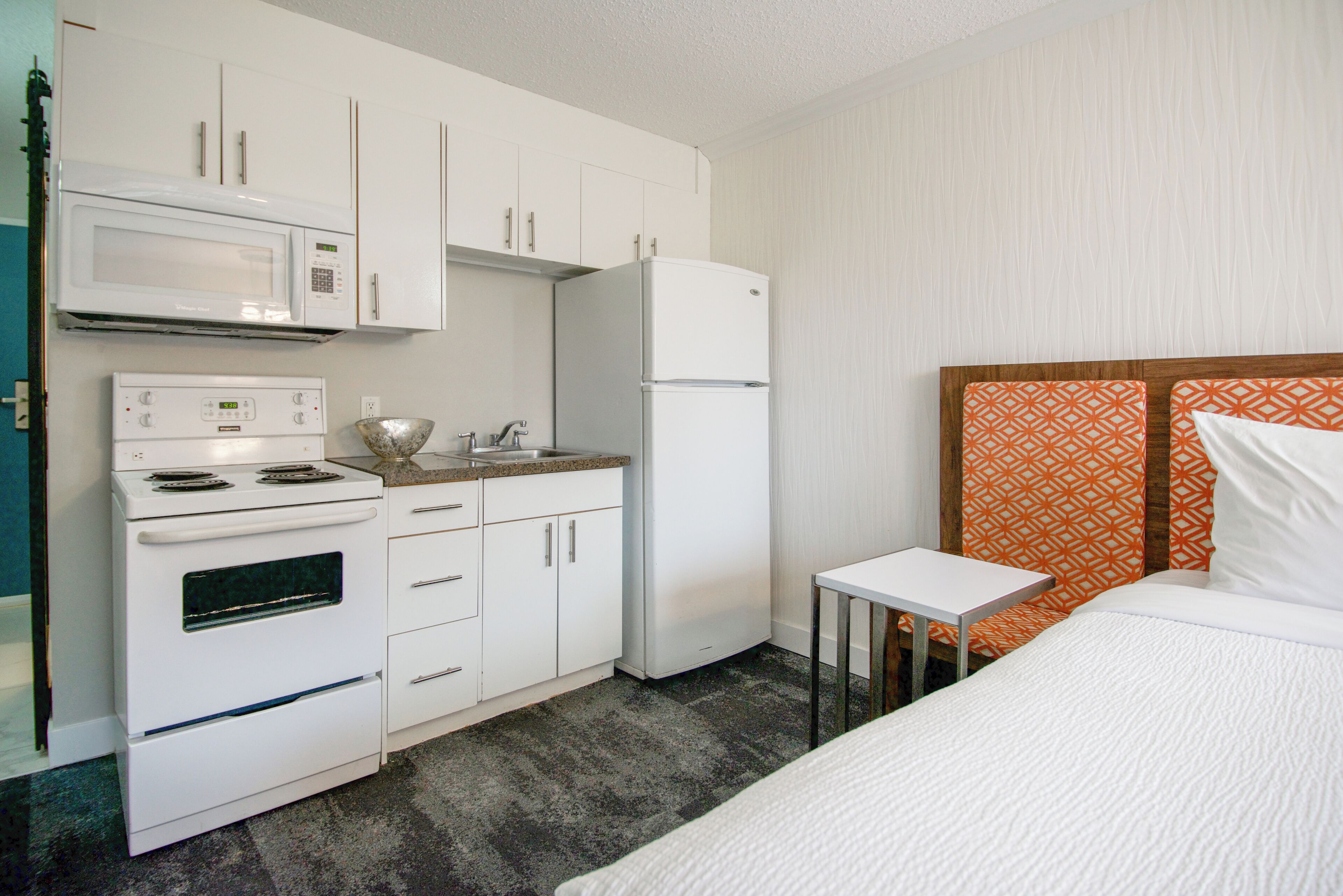Habitación de hotel compacta con kitchenette que incluye microondas, estufa y refrigerador.