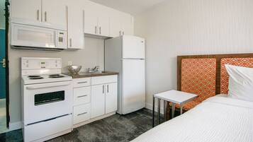 Habitación de hotel compacta con kitchenette que incluye microondas, estufa y refrigerador.