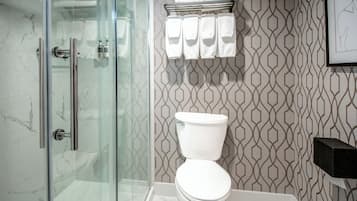 A bathroom with a glass shower enclosure, a toilet, and a towel rack with multiple towels.