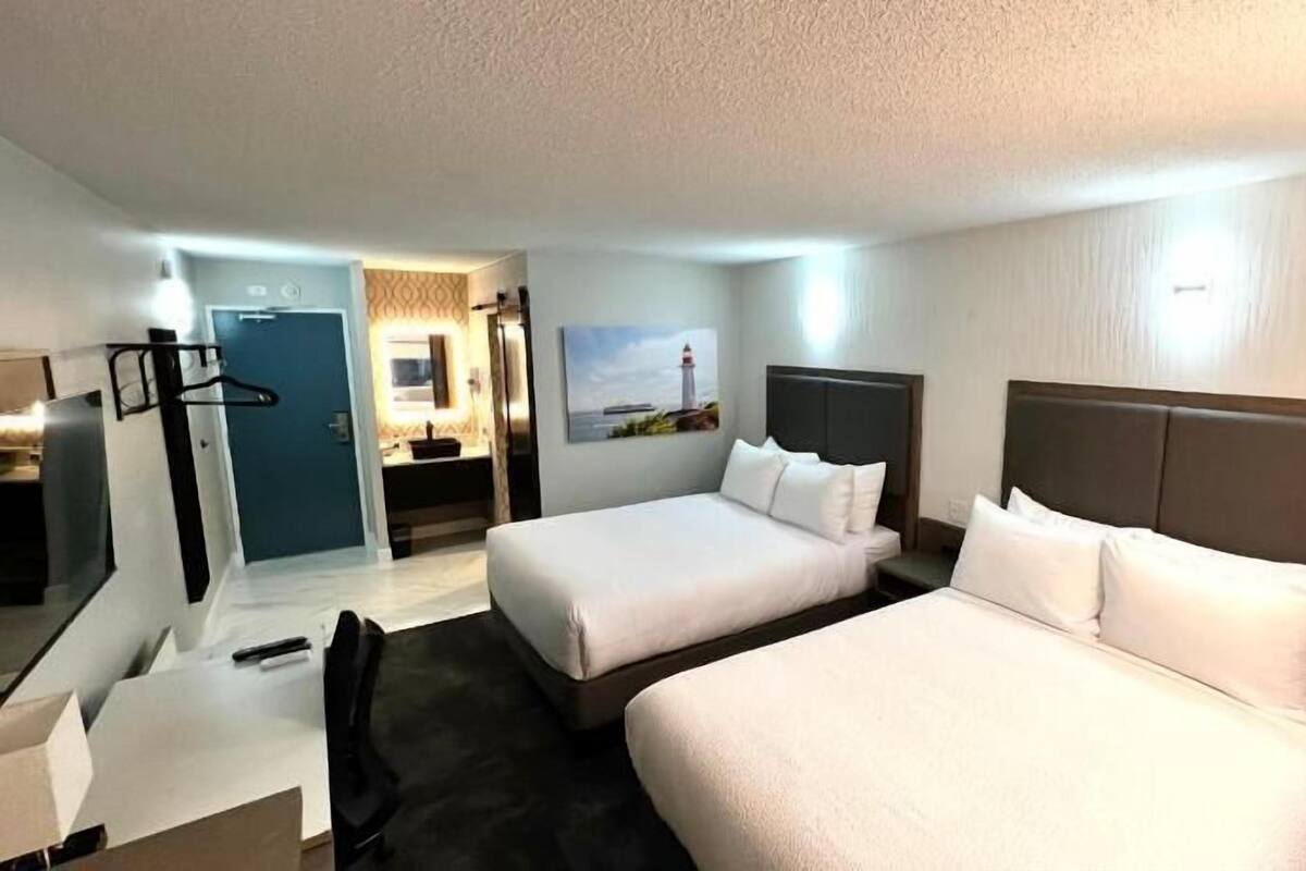 A hotel room with two beds, a desk, a chair, a mirror, and a bathroom visible through an open door.
