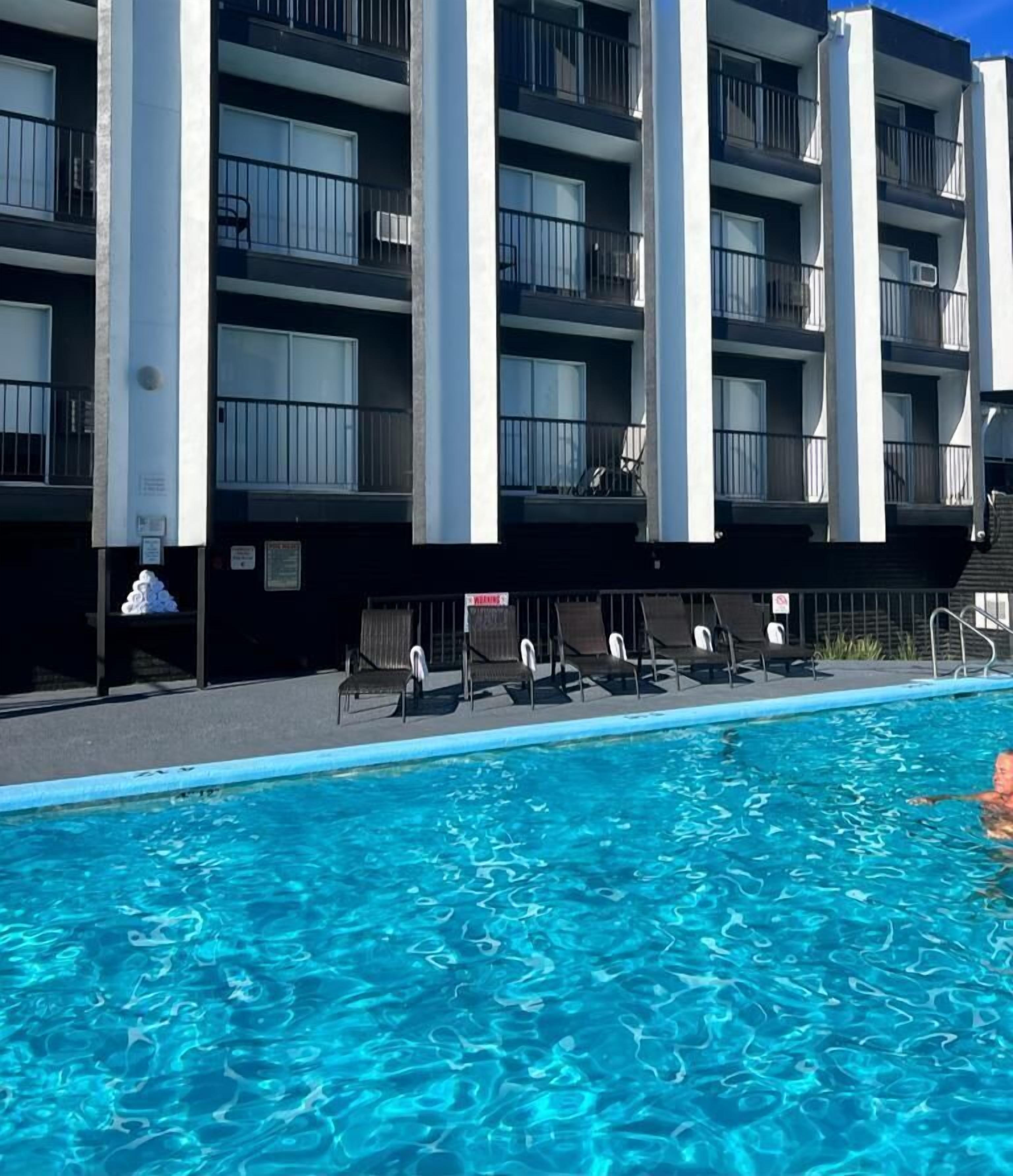 Una piscina con sillones de descanso y un edificio con balcones al fondo.