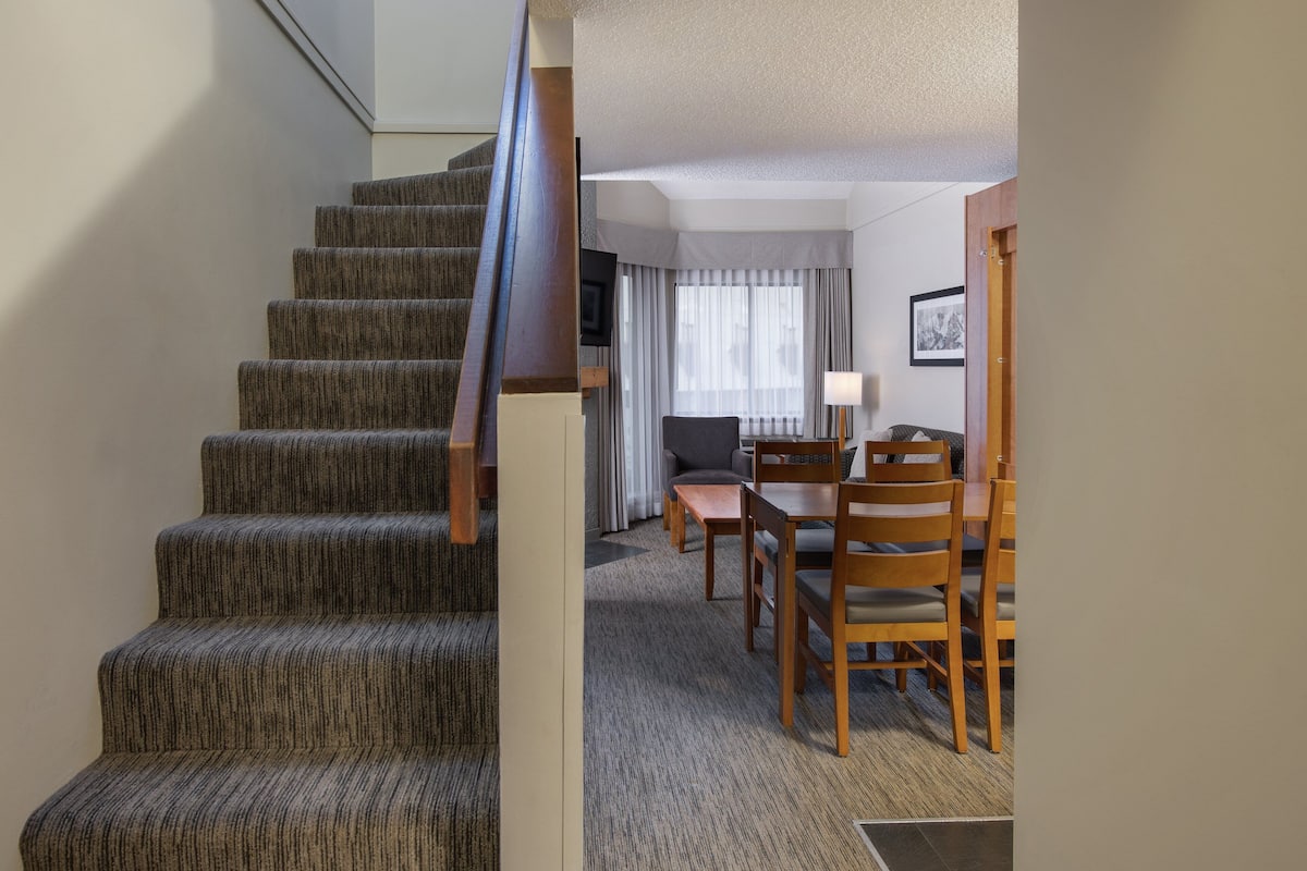 A staircase leading to a living area with a sofa, a dining table, and chairs.