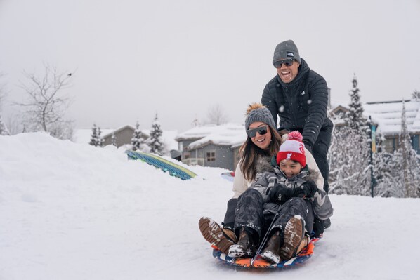 A family sledding down a snowy slope with houses in the background.