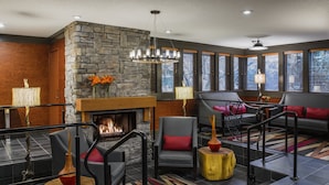A modern living room with a stone fireplace, comfortable seating, and large windows. - Whistler Village Inn And Suites (Whistler)