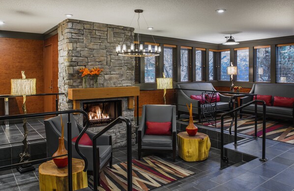 A modern living room with a stone fireplace, comfortable seating, and large windows. - Whistler Village Inn And Suites (Whistler)