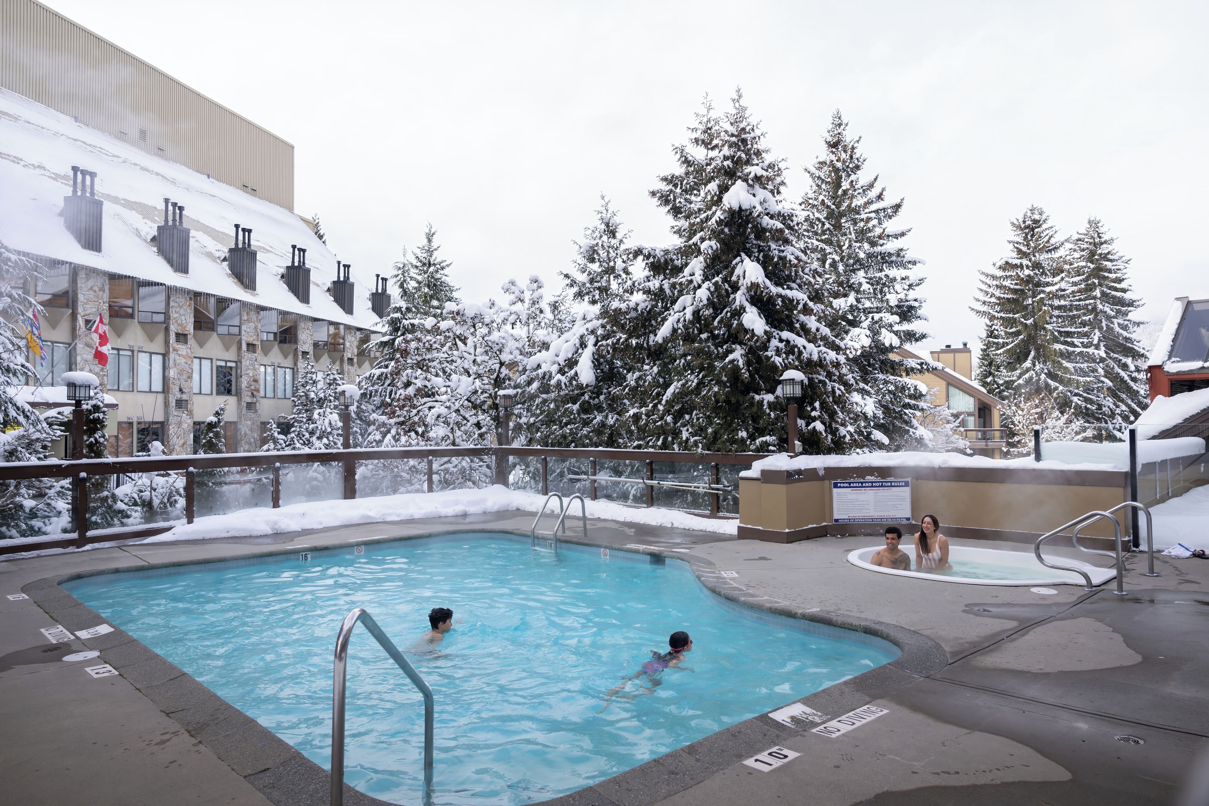 Ein Poolbereich mit einem klaren, blauen Pool, umgeben von schneebedeckten Bäumen und Gebäuden.
