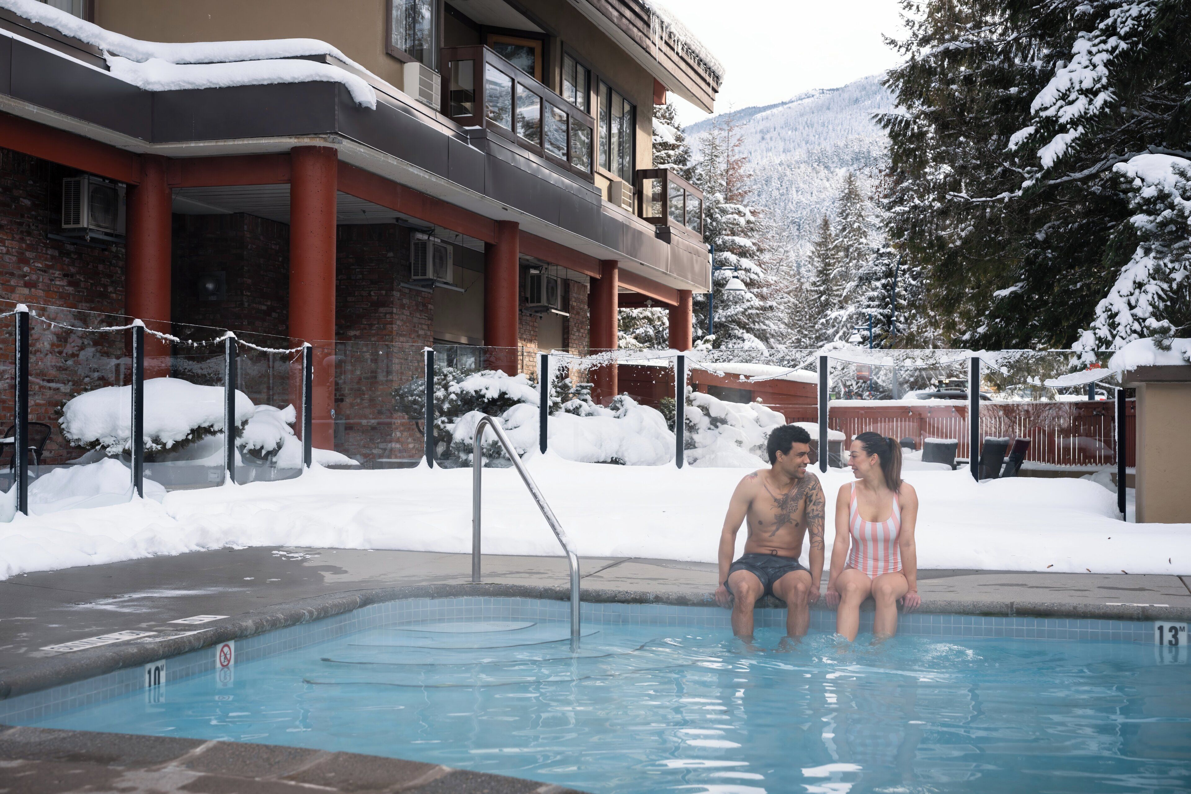 Un área de piscina con vistas despejadas del paisaje nevado circundante y un edificio con balcón.