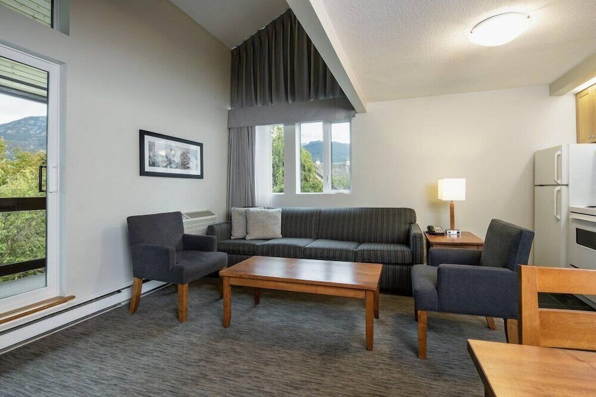 A modern living room with a sofa, two armchairs, a coffee table, a lamp, and a refrigerator.