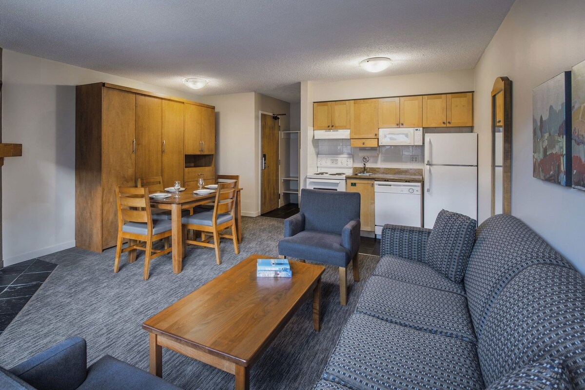 A compact living space with a dining area, sofa, coffee table, kitchen, and fireplace.