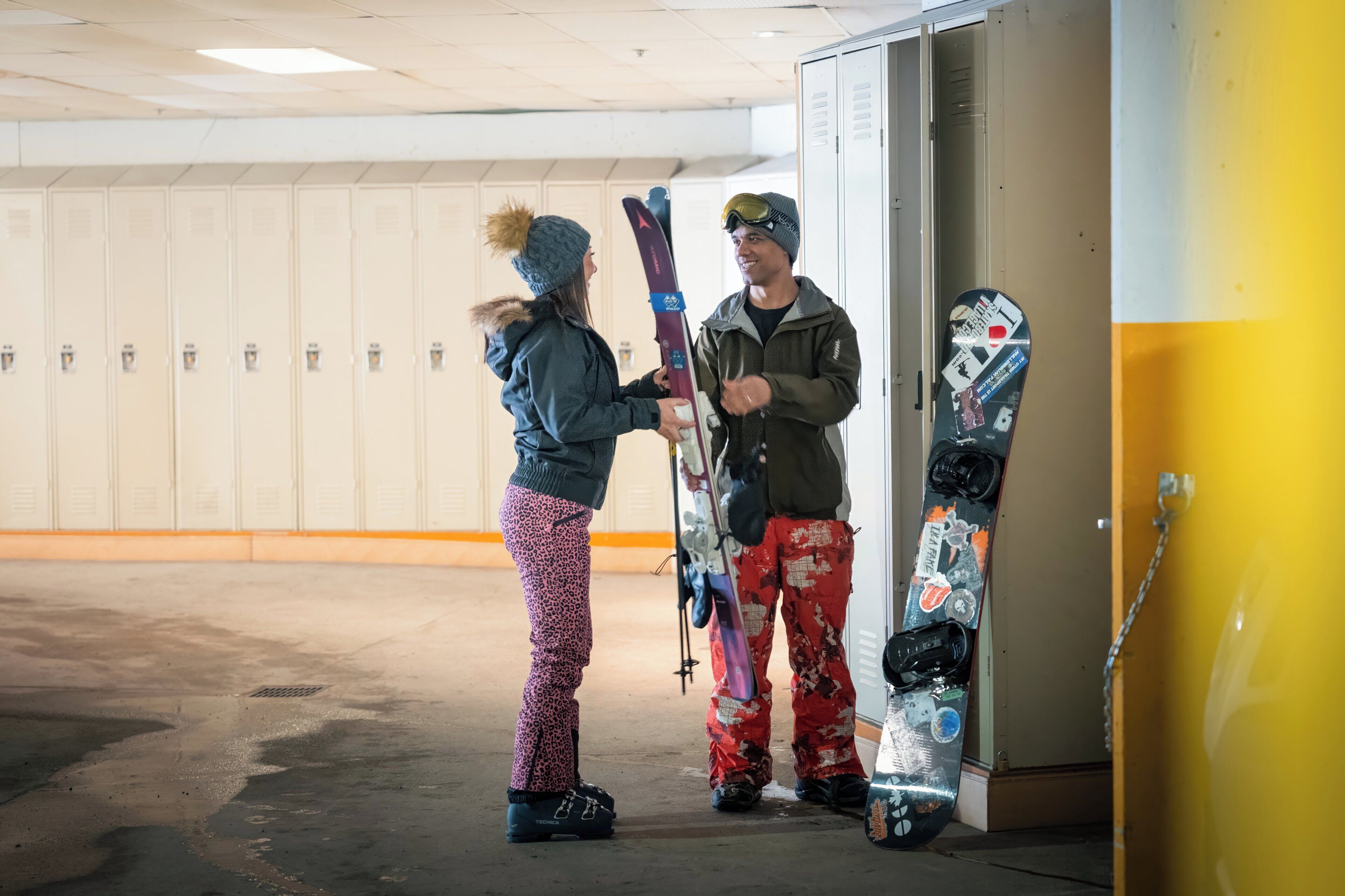A person holding a snowboard in a hallway with lockers.