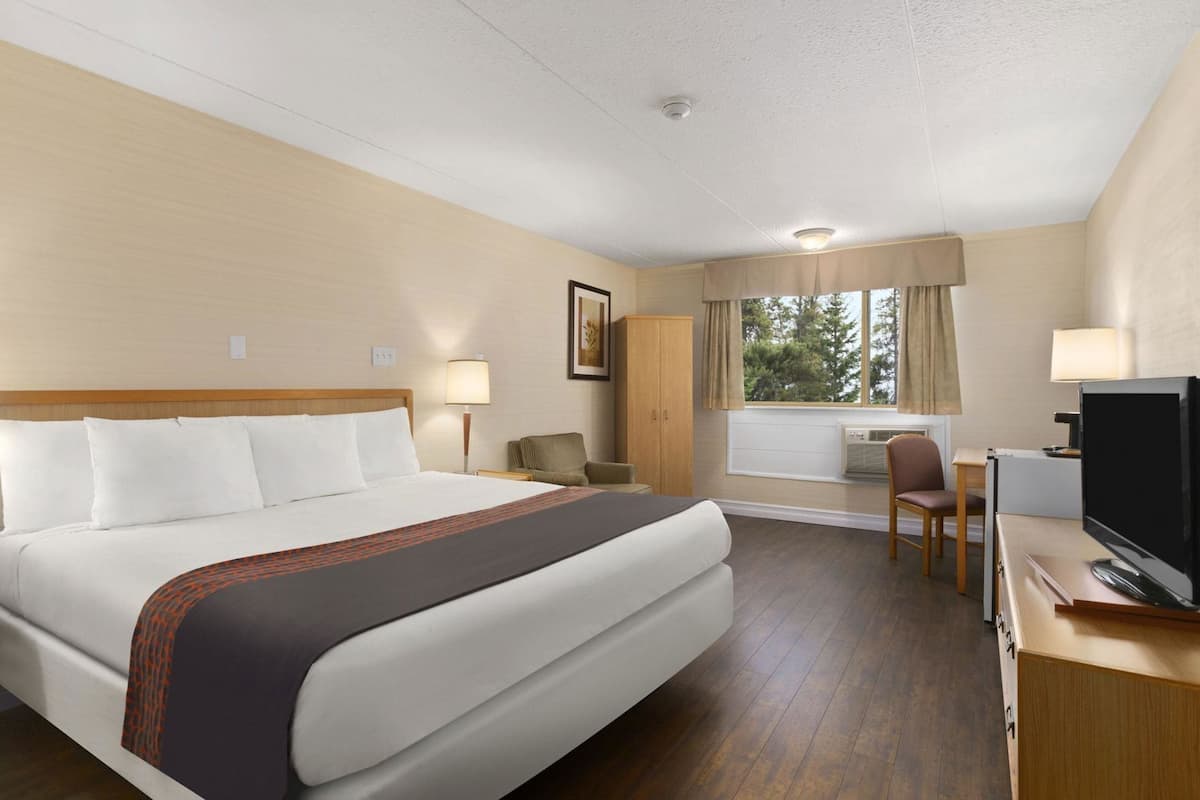 A hotel room with a large bed, a desk with a chair, a television, and a window with curtains.