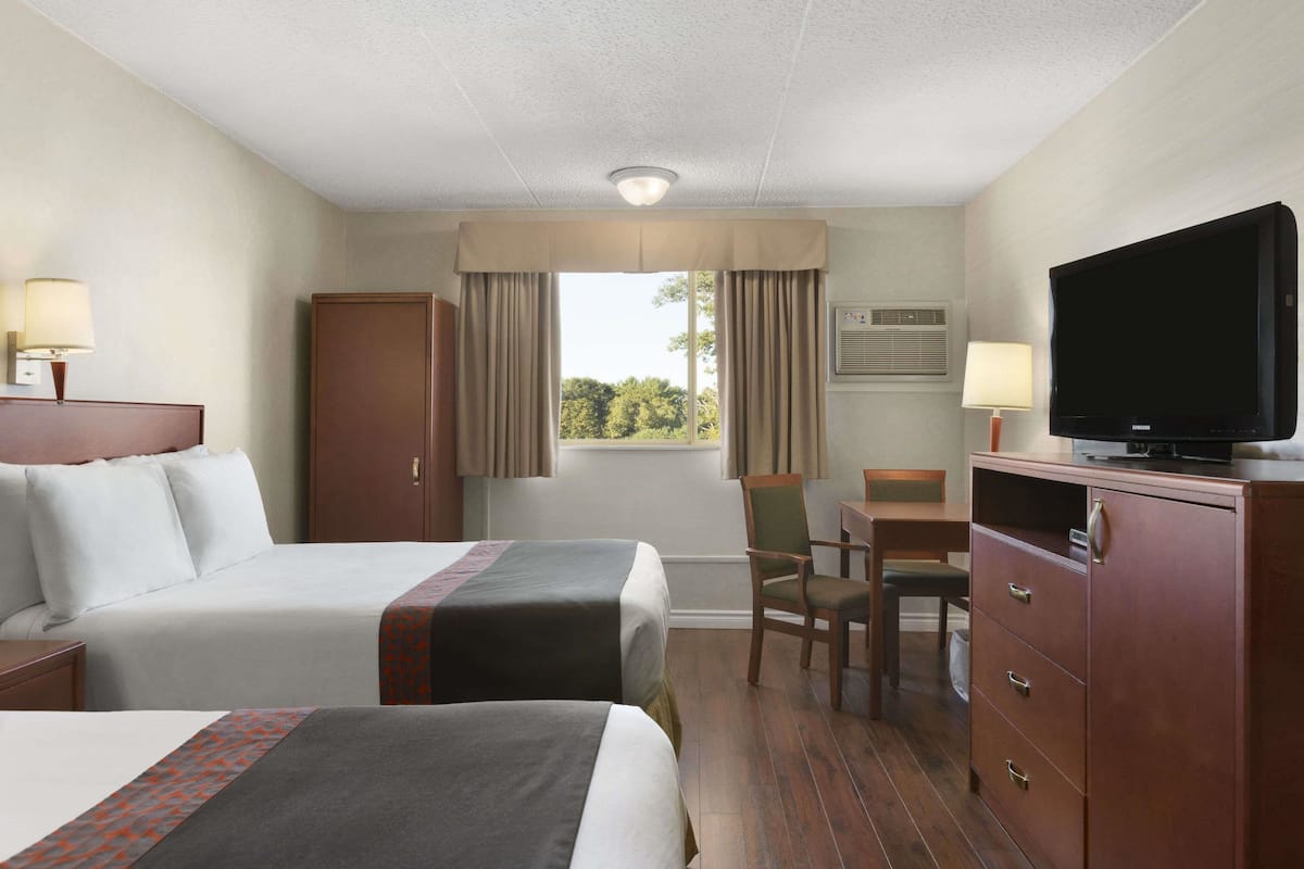 A hotel room with two beds, a desk, a television, and a window with curtains.
