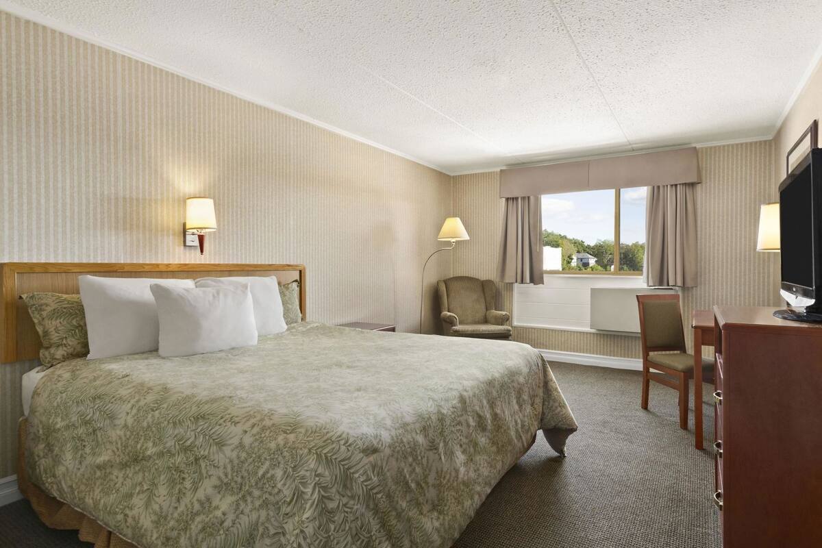 A hotel room with a large bed, a desk, a chair, a television, and a window with curtains.