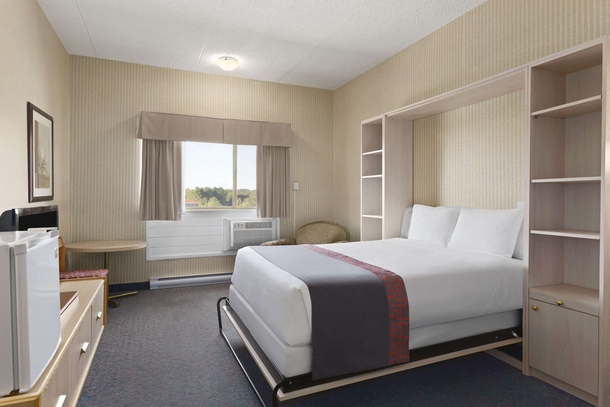 A hotel room with a bed, a desk, a chair, a wardrobe, and a window with curtains.