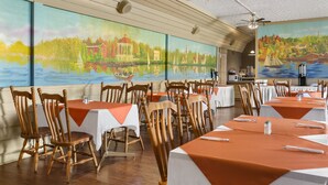 A dining area with wooden chairs and tables, large paintings on the walls, and ceiling fans.