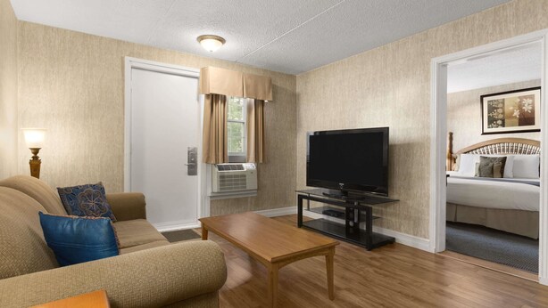 A compact living room with a sofa, a coffee table, a flat-screen TV, and a bed in the adjacent room.
