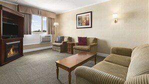 A hotel room with a fireplace, a television, two armchairs, a sofa, a coffee table, and a framed picture on the wall.