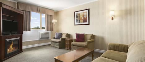 A hotel room with a fireplace, a television, two armchairs, a sofa, a coffee table, and a framed picture on the wall.