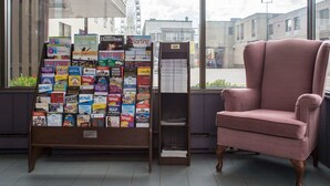 A travel agency office with a large display of brochures and a pink armchair.