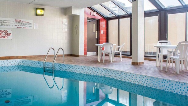 An indoor swimming pool with a tiled floor, a safety sign, and a glass door leading to an exit.