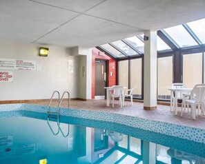 Una piscina interior con suelo de baldosas, un cartel de seguridad y una puerta de cristal que da a una salida.