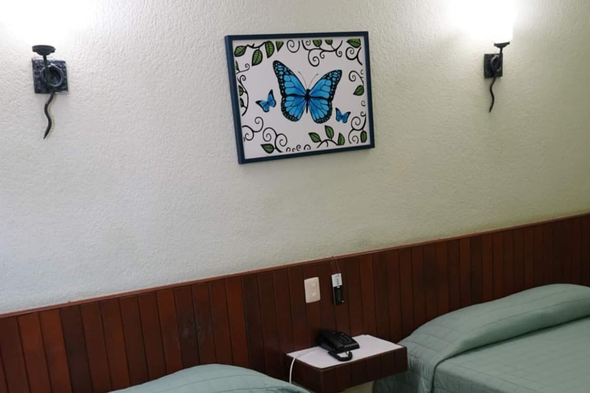 A hotel room with two beds, a wooden headboard, a wall-mounted telephone, and a framed butterfly artwork.