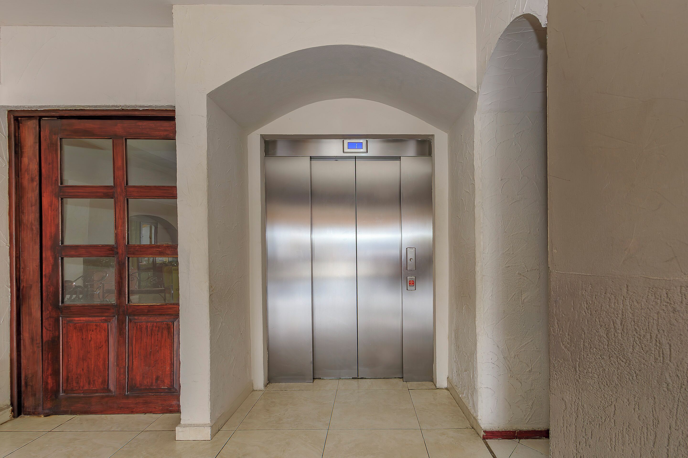 An elevator with a digital display, a wooden door to the left, and a tiled floor.