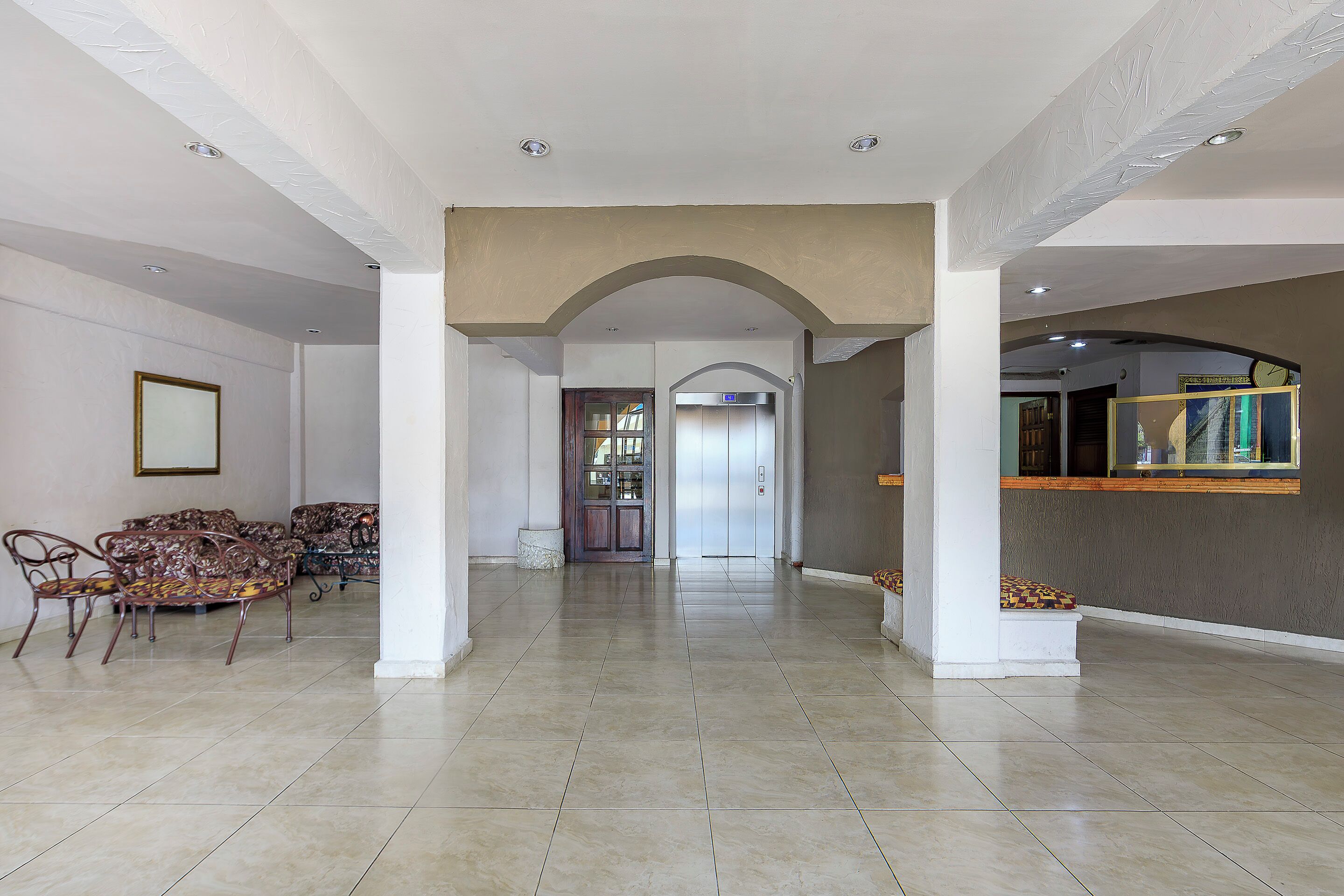 Um hall espaçoso com teto alto, piso de azulejos e um arco central que dá acesso a um elevador.