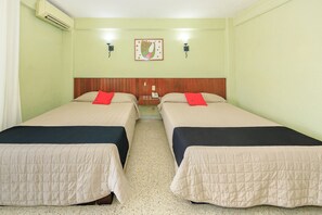 A room with two beds, each with a headboard, a small table with a telephone, and a wall-mounted light fixture.