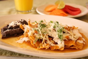 A plate of nachos topped with shredded chicken and cheese, accompanied by a side of black pudding and a plate of sliced carrots and tomatoes. - Palette Hotel Batab (Cancun)