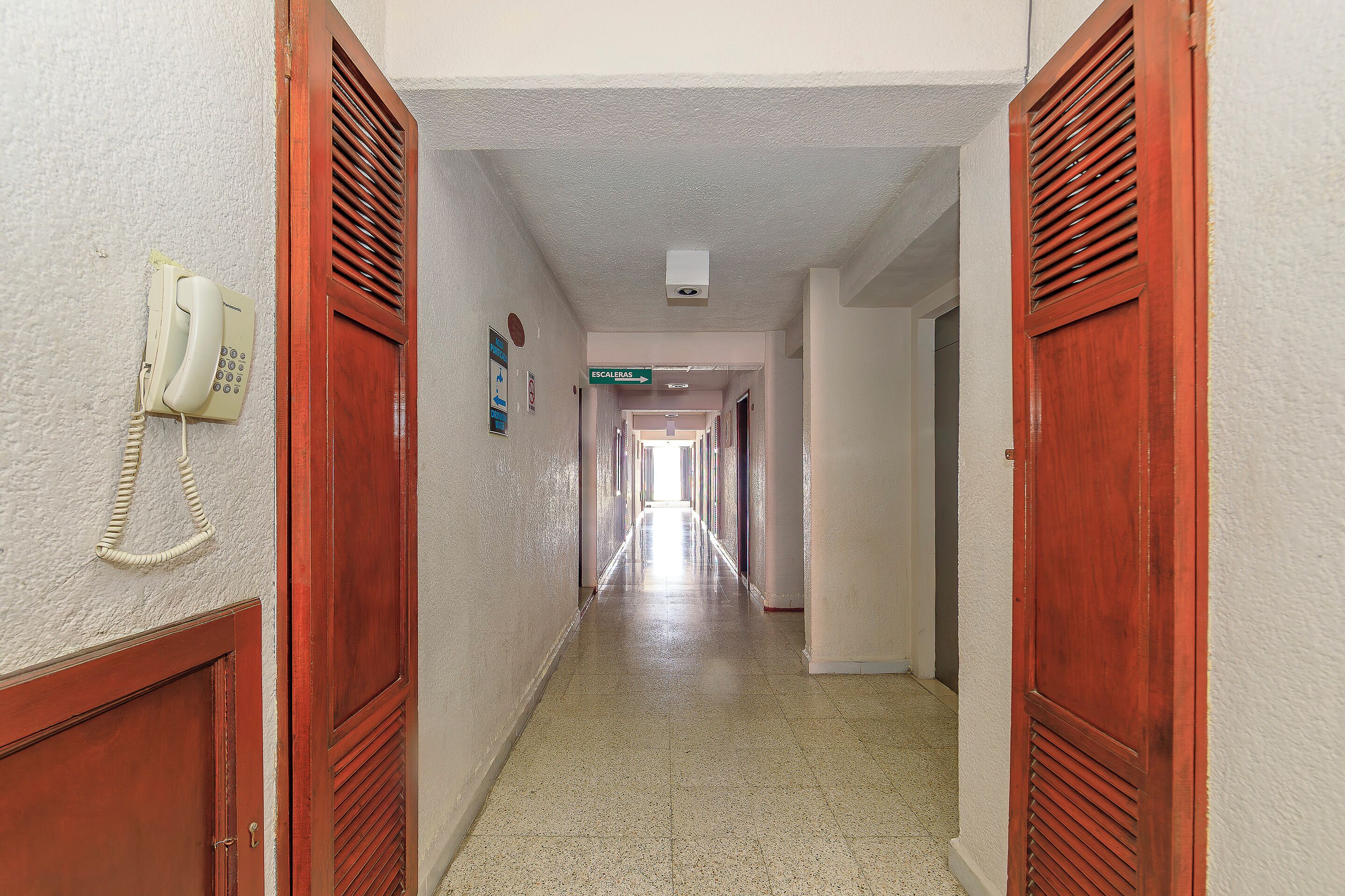 Um corredor com portas de madeira, um telefone e placas de sinalização.