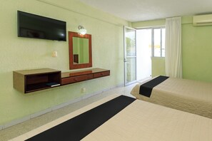 A hotel room with a flat-screen TV mounted on the wall, a wooden bedside table with a mirror, a bed with a black and beige bedspread, and a sliding glass door leading to a balcony. - Palette Hotel Batab (Cancun)