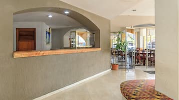 A hotel lobby with a reception desk, a clock, a plant, and a seating area.