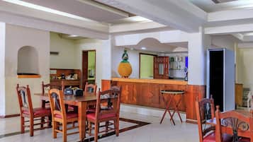 A dining area with a wooden table and chairs, a kitchen in the background, and a bar area with a pineapple decoration.