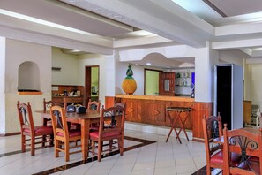 A dining area with a wooden table and chairs, a kitchen in the background, and a bar area with a pineapple decoration.