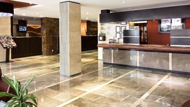 A modern hotel lobby with a reception desk, a large pillar, and a television screen. - Hotel Metropol (Mexico City)