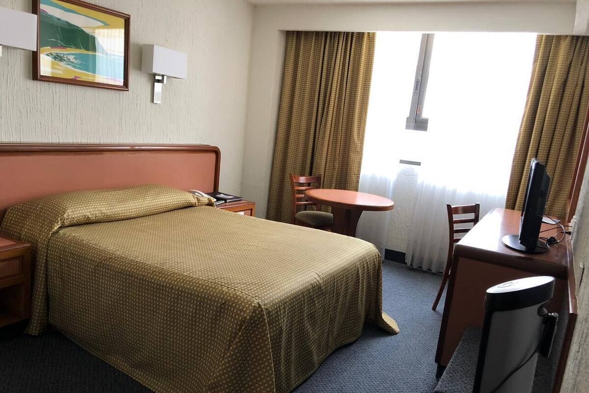 A hotel room with a bed, a desk, a chair, a television, and a window with curtains.