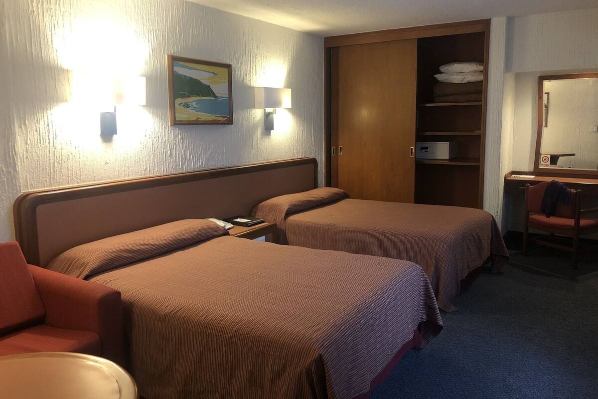 A hotel room with two beds, a desk, a chair, a wardrobe, and a painting on the wall.