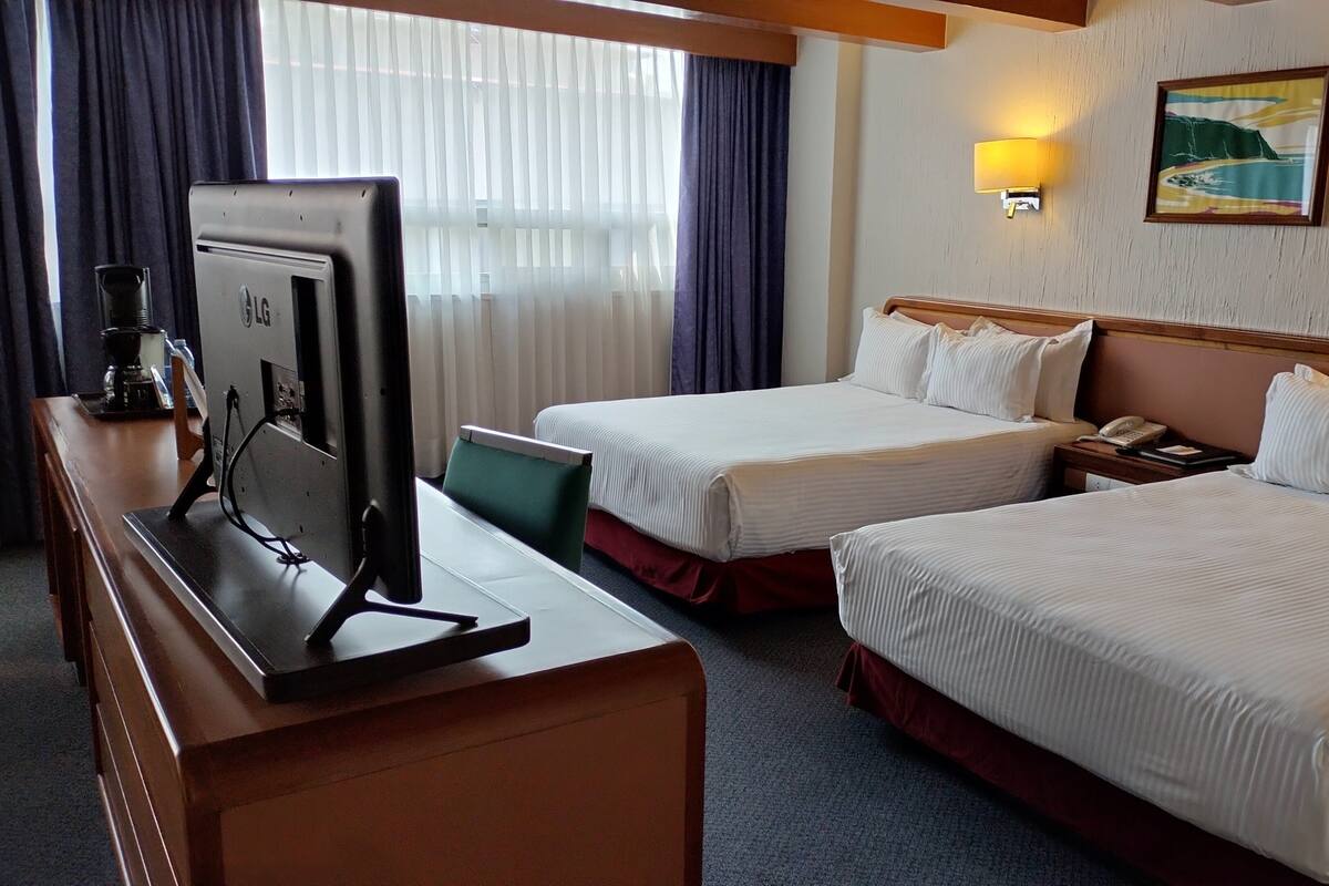 A hotel room with two beds, a desk with a computer, a telephone, and a painting on the wall.