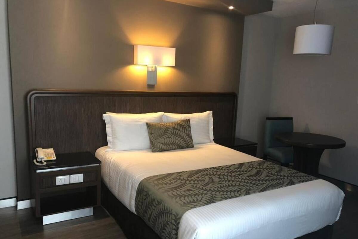 A neatly made bed with a patterned bedspread, a bedside telephone, and a wall-mounted lamp.