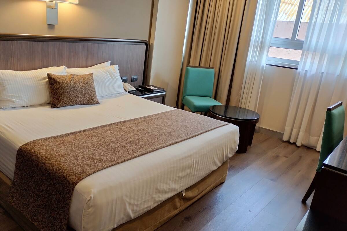 A hotel room with a large bed, a bedside table, a chair, and a small table.